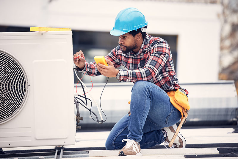 5 Benefits of Planned Commercial HVAC Maintenance. Air conditioner, cables and technician man ac repair, maintenance or working on electrical power generator. African person, electrician or contractor with electricity, heat pump check and engineering.