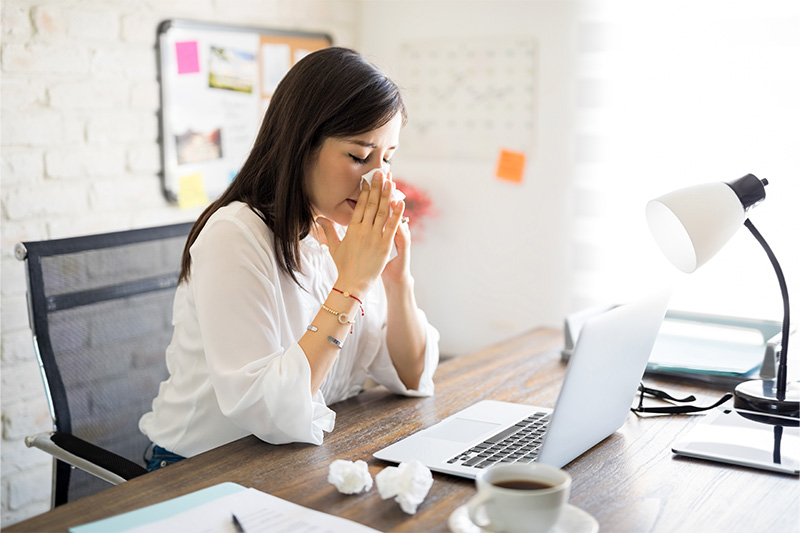 Woman blowing her nose at a desk.