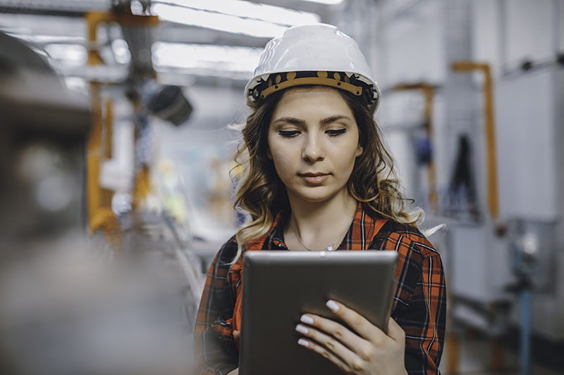 Woman in protective clothing in factoryYoung electrical engineer woman using touchpad with digital tablet and standing in front of control panel working about technical problems and writes the results of measurements in control room of modern thermal or nuclear power plant electric energy station.